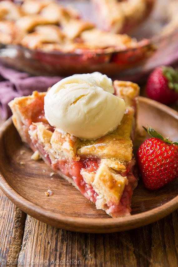 slice of strawberry rhubarb pie with a scoop of ice cream on top on a wood plate