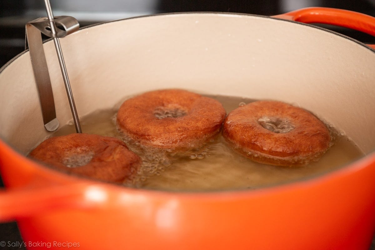 frying 3 doughnuts in oil in orange pot.