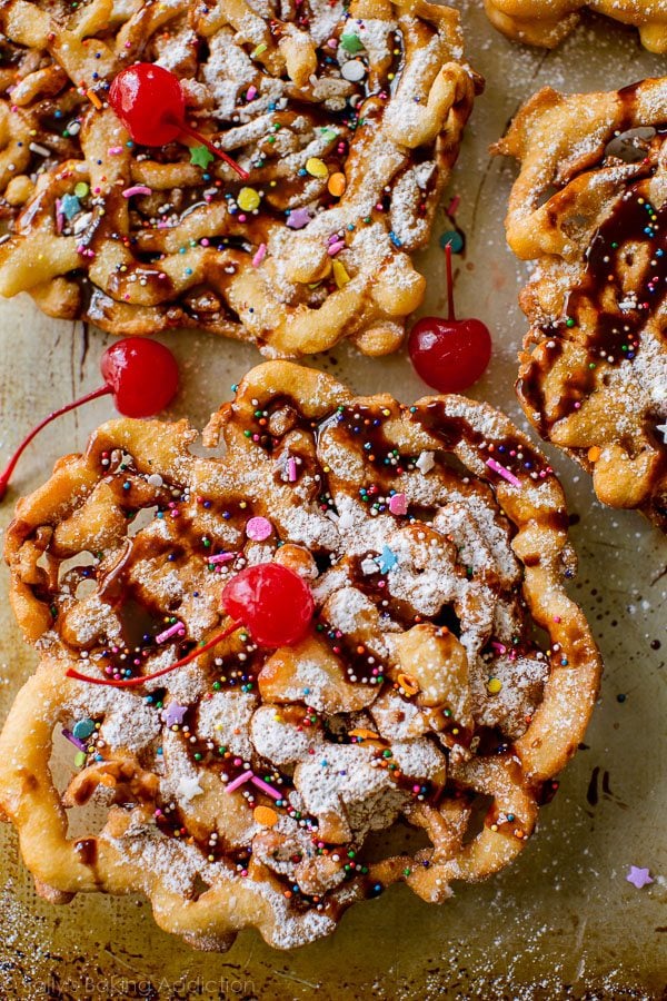 overhead image of funnel cakes topped with confectioners' sugar, chocolate sauce, sprinkles, and cherries