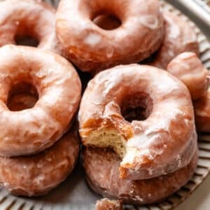 doughnuts piled on gray plate with one with bite taken out.