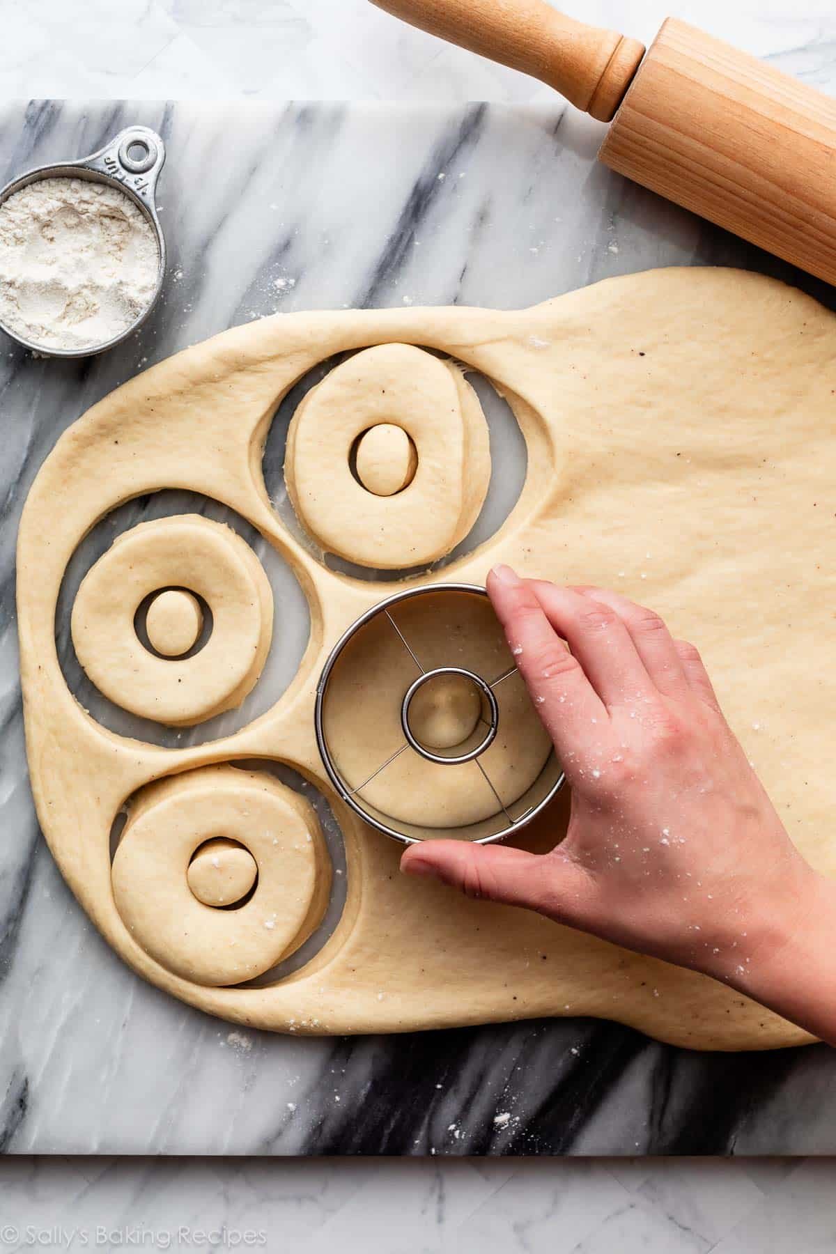 hand using cutter to shape dough on marble counter.