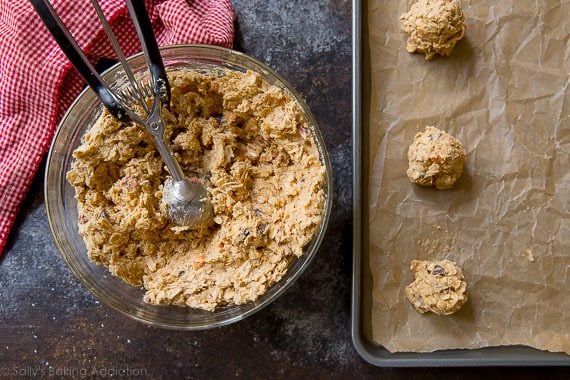 cookie dough in a glass bowl with a cookie scoop and cookie dough balls on a baking sheet