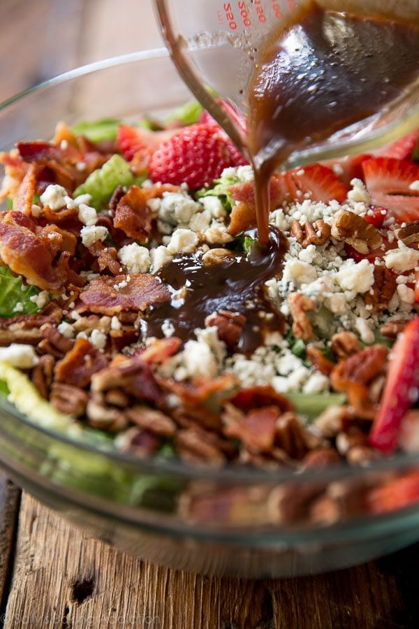 pouring dressing onto strawberry bacon salad in a glass bowl