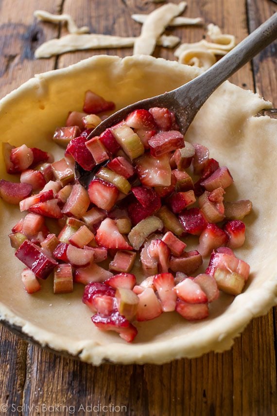 strawberry rhubarb pie filling in a pie dish with a wood spoon