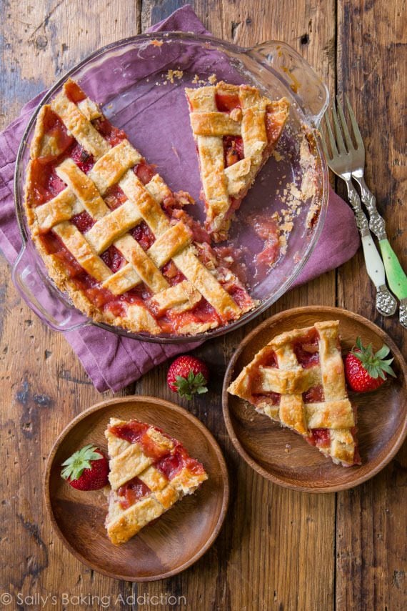overhead image of strawberry rhubarb pie in a glass pie dish and slices of pie on wood plates