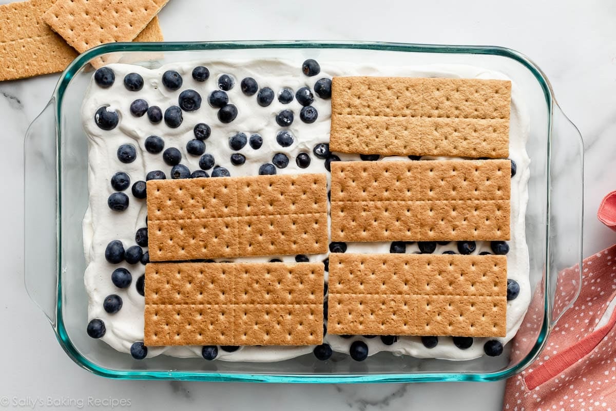 graham crackers arranged on top of blueberries and whipped cream in glass baking dish.