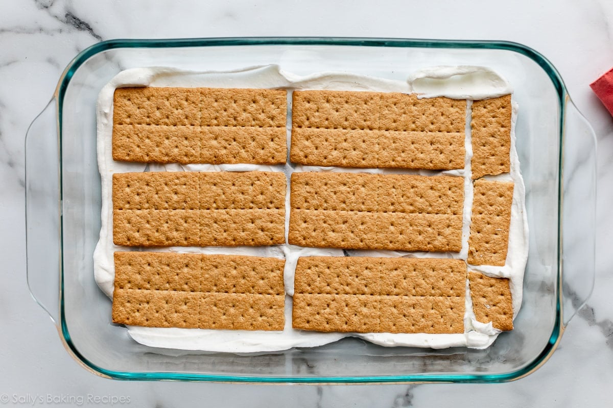 graham crackers arranged on top of whipped cream in glass baking dish.