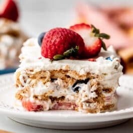 slice of berry icebox cake with vanilla whipped cream between the layers on white plate.