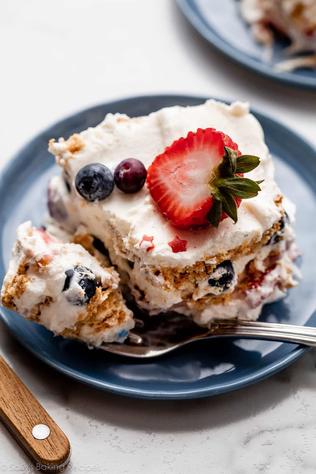slice of icebox cake with vanilla whipped cream between the layers and strawberry and blueberries on top.