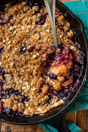 overhead image of blueberry peach crisp in a skillet with a spoon
