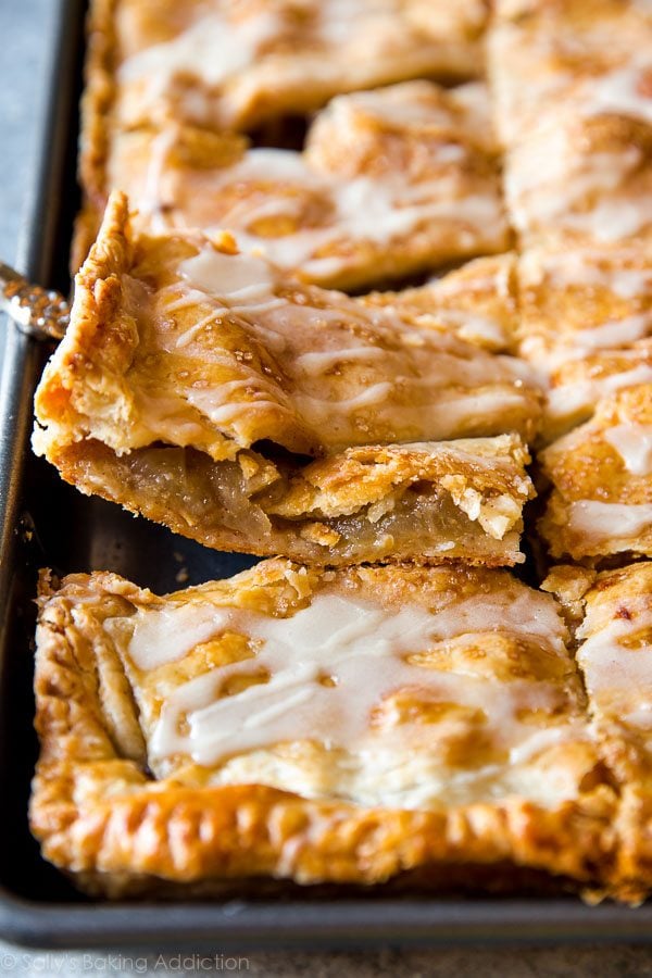 apple slab pie in a pan with a slice being removed on a pie server