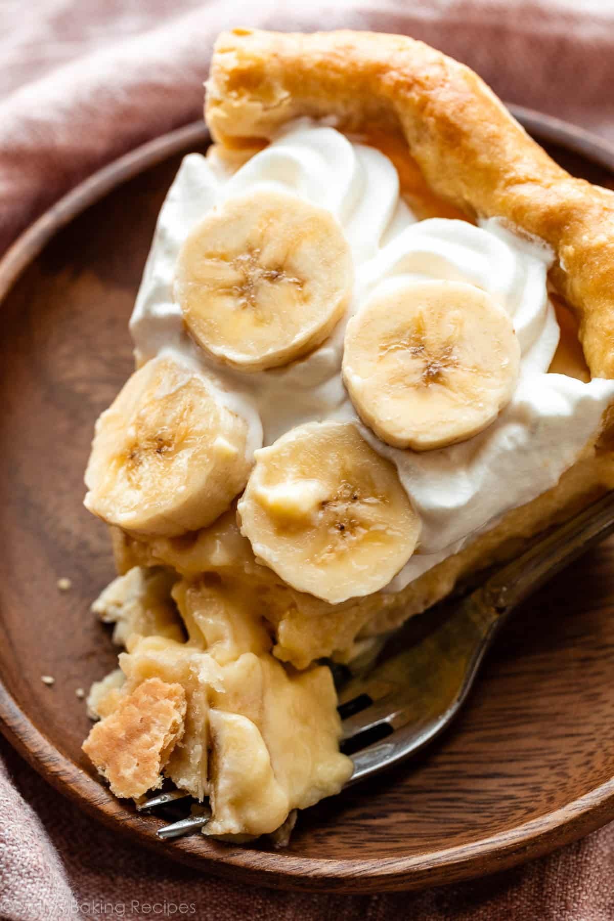 slice of banana cream pie with whipped cream on wooden plate.