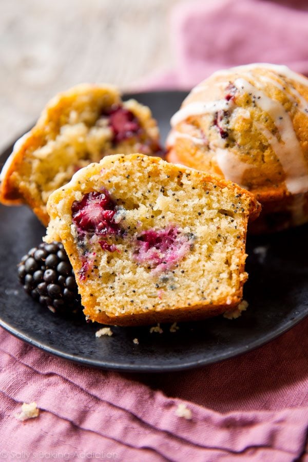 blackberry lemon poppy seed muffins on a black plate with one cut in half showing the inside