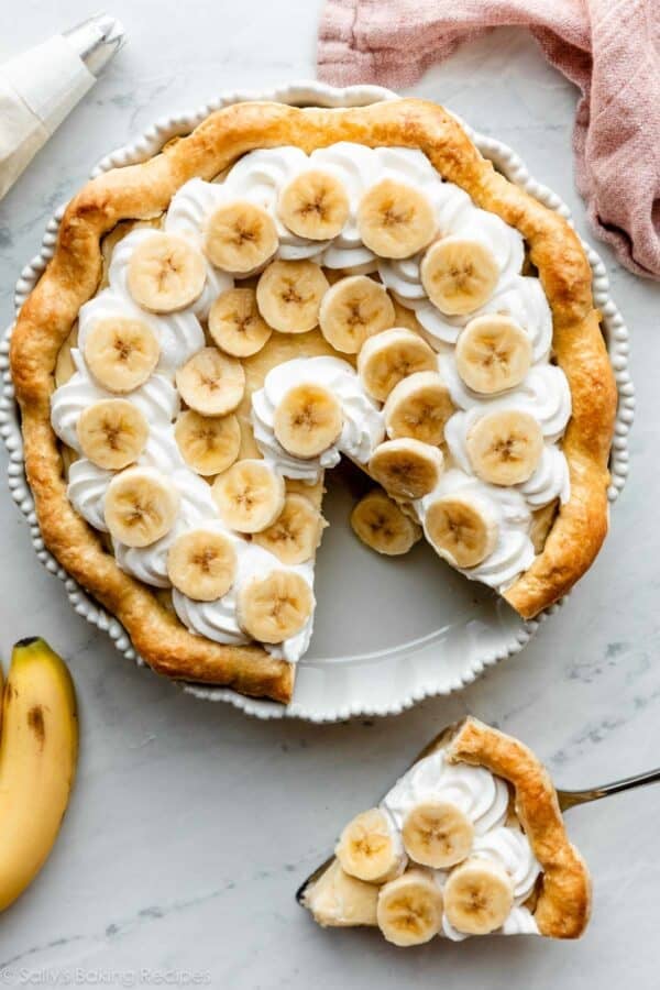 overhead photo of banana cream pie with 1 slice removed and sitting on the counter below it.