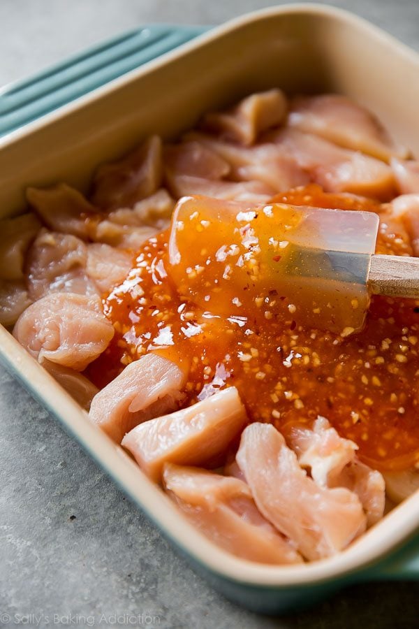 spreading sweet chili sauce onto pieces of chicken in a baking dish