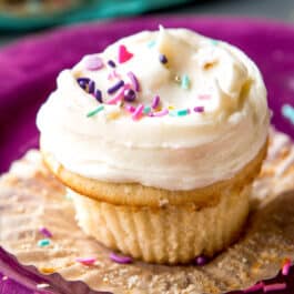 Vanilla cupcake with vanilla frosting and sprinkles on a purple plate