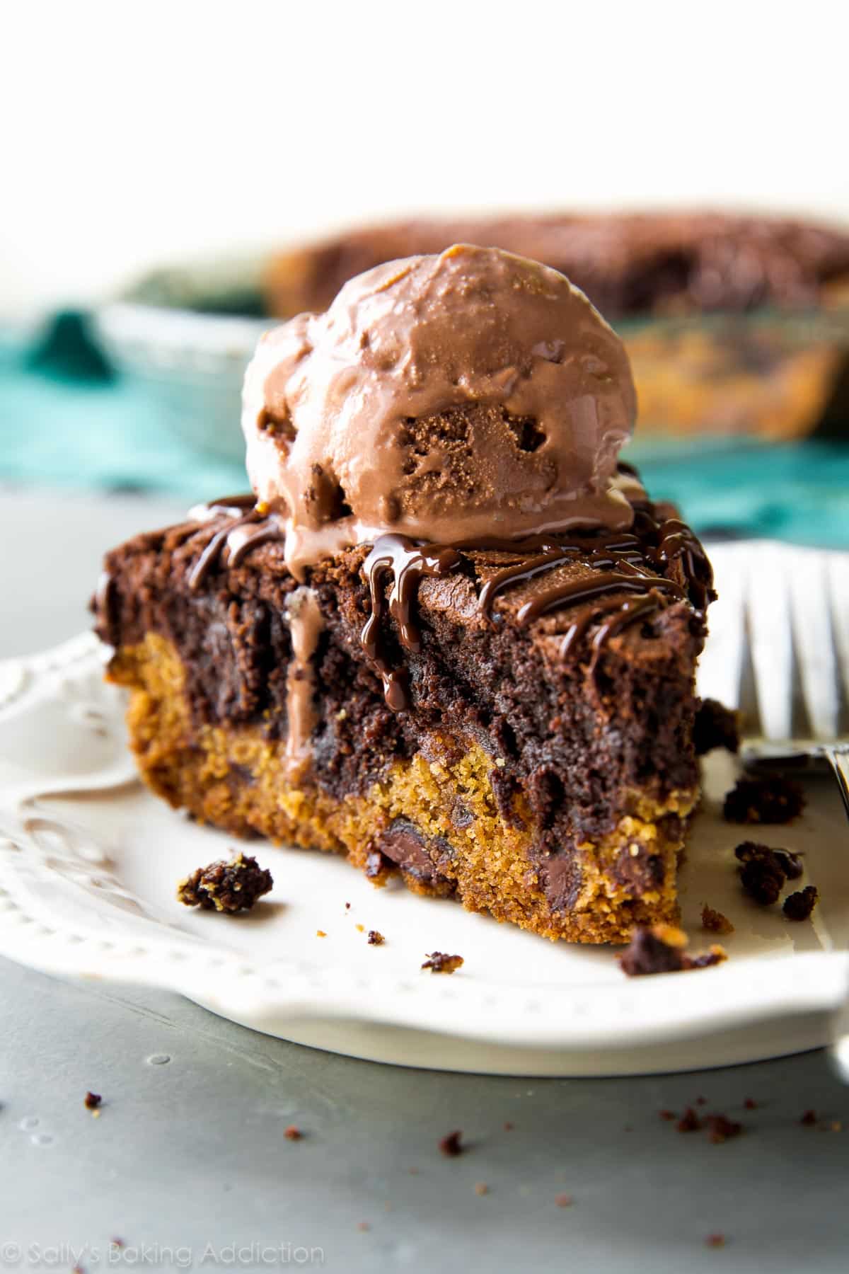 slice of brookie pie with a scoop of chocolate ice cream on top on a white plate with a fork