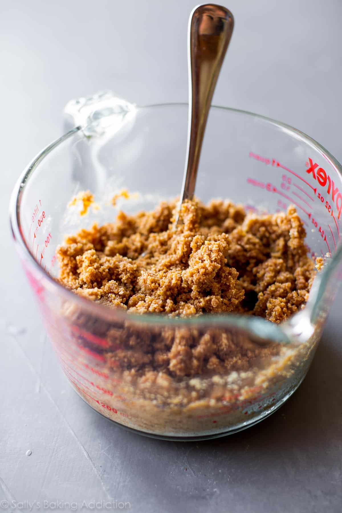 graham cracker pie crust mixture in a glass measuring cup with a spoon