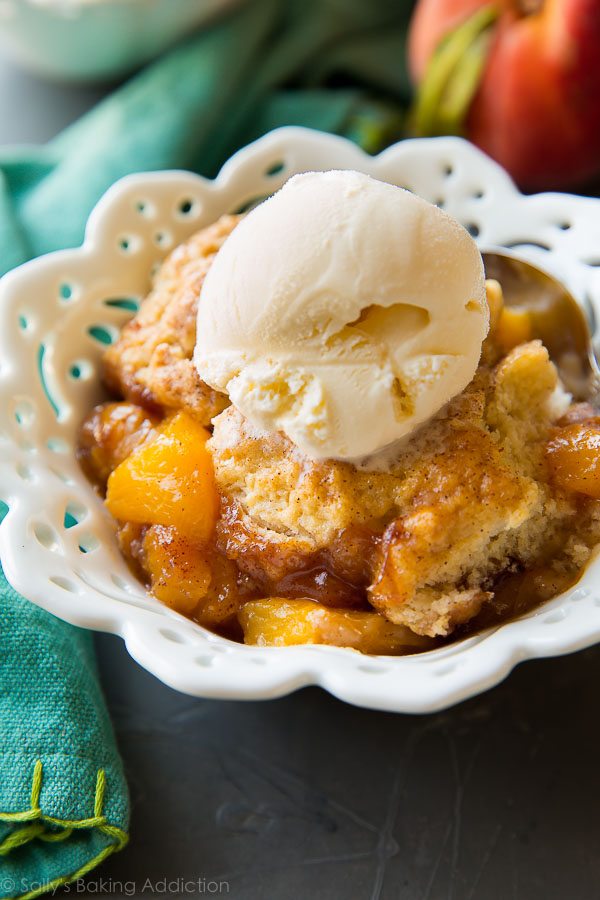 peach cobbler topped with a scoop of vanilla ice cream in a white bowl