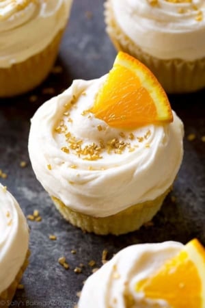 mimosa cupcakes topped with champagne frosting, an orange slice, and gold sprinkles