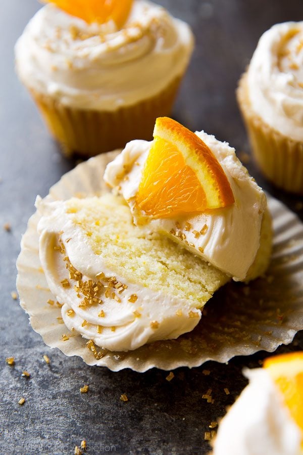 mimosa cupcake cut in half topped with champagne frosting, an orange slice, and gold sprinkles
