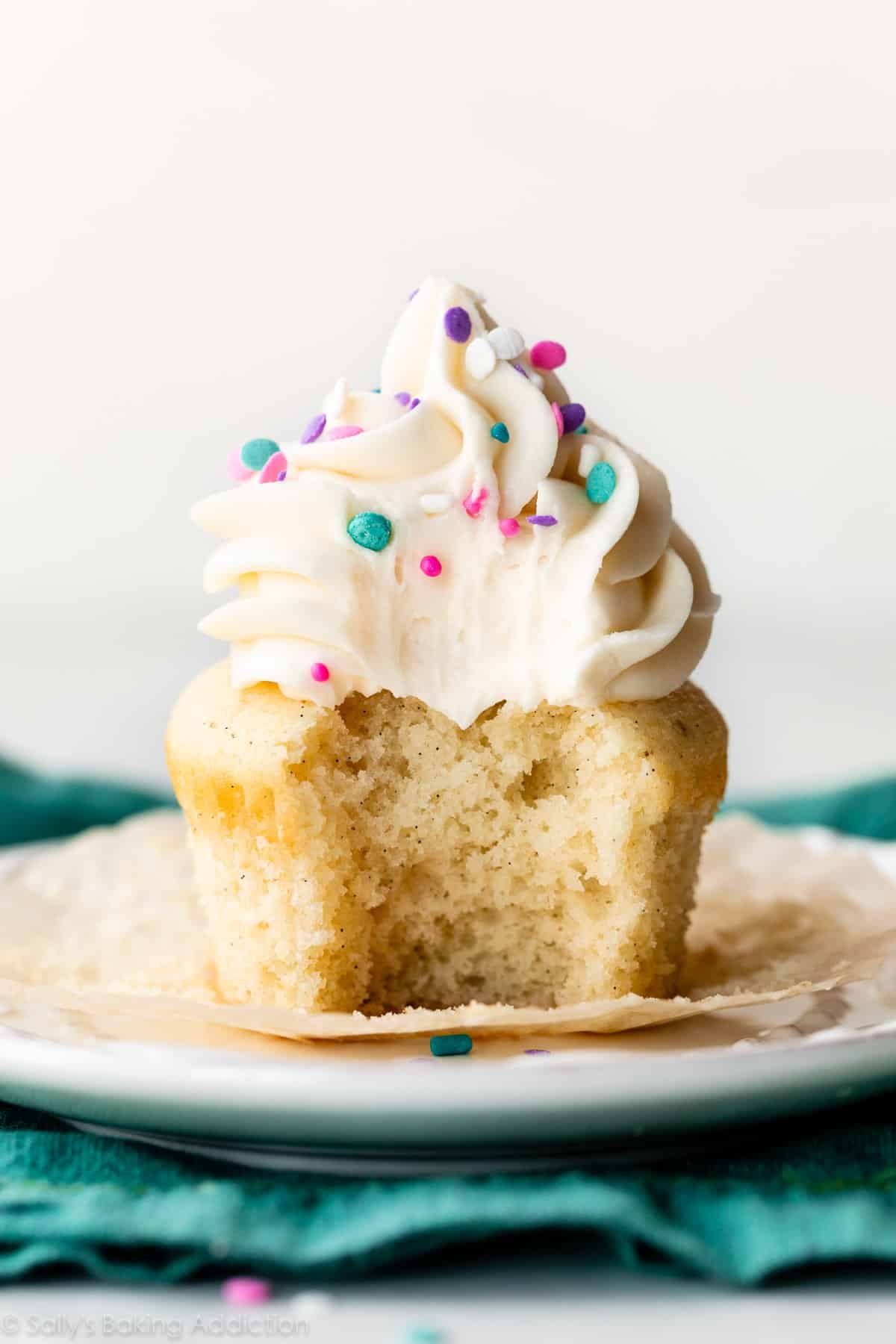 one vanilla cupcake topped with vanilla buttercream with bite taken out.