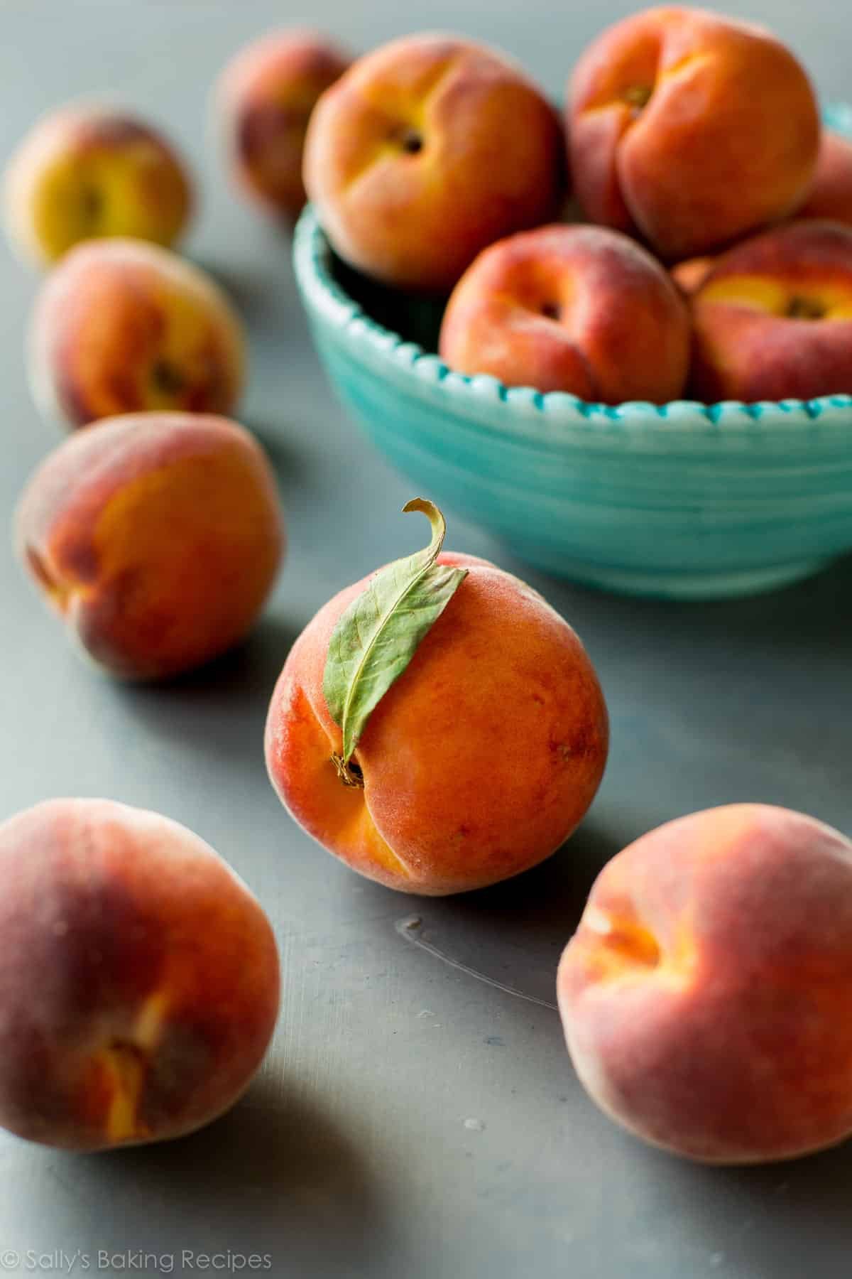 fresh peaches on gray backdrop with some in a blue bowl.