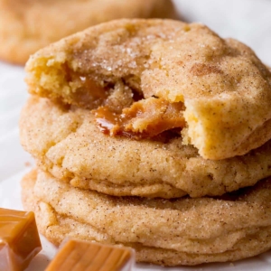 stack of caramel snickerdoodle cookies with one broken in half showing the caramel inside