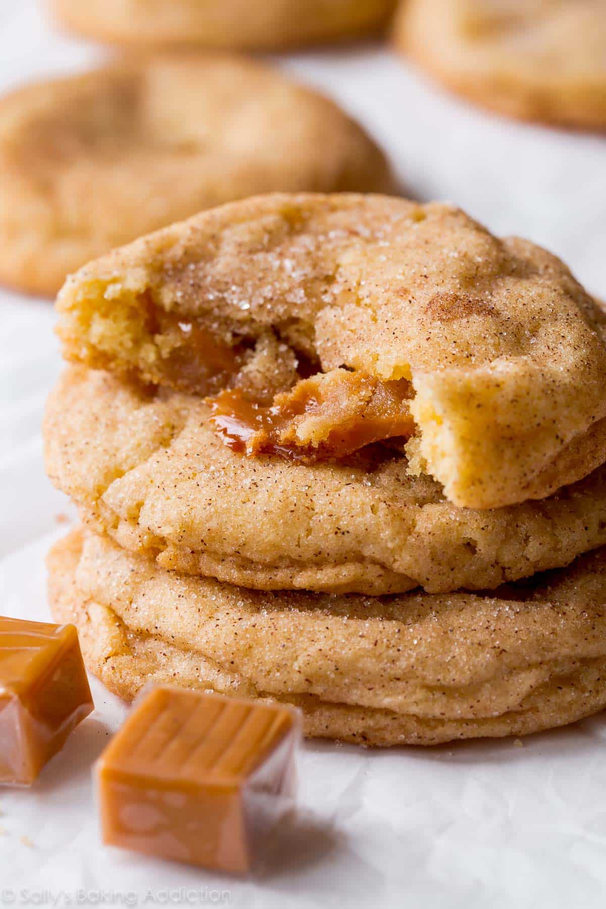 stack of caramel snickerdoodle cookies with one broken in half showing the caramel inside