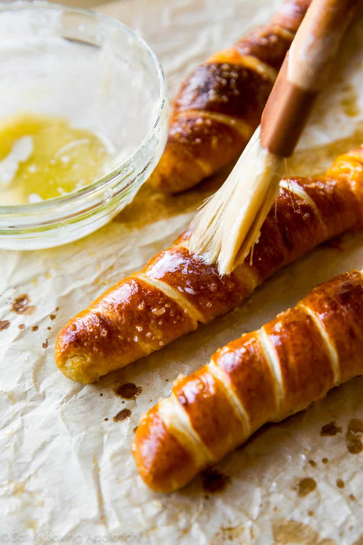 brushing baked cheesy pretzel twists with melted butter