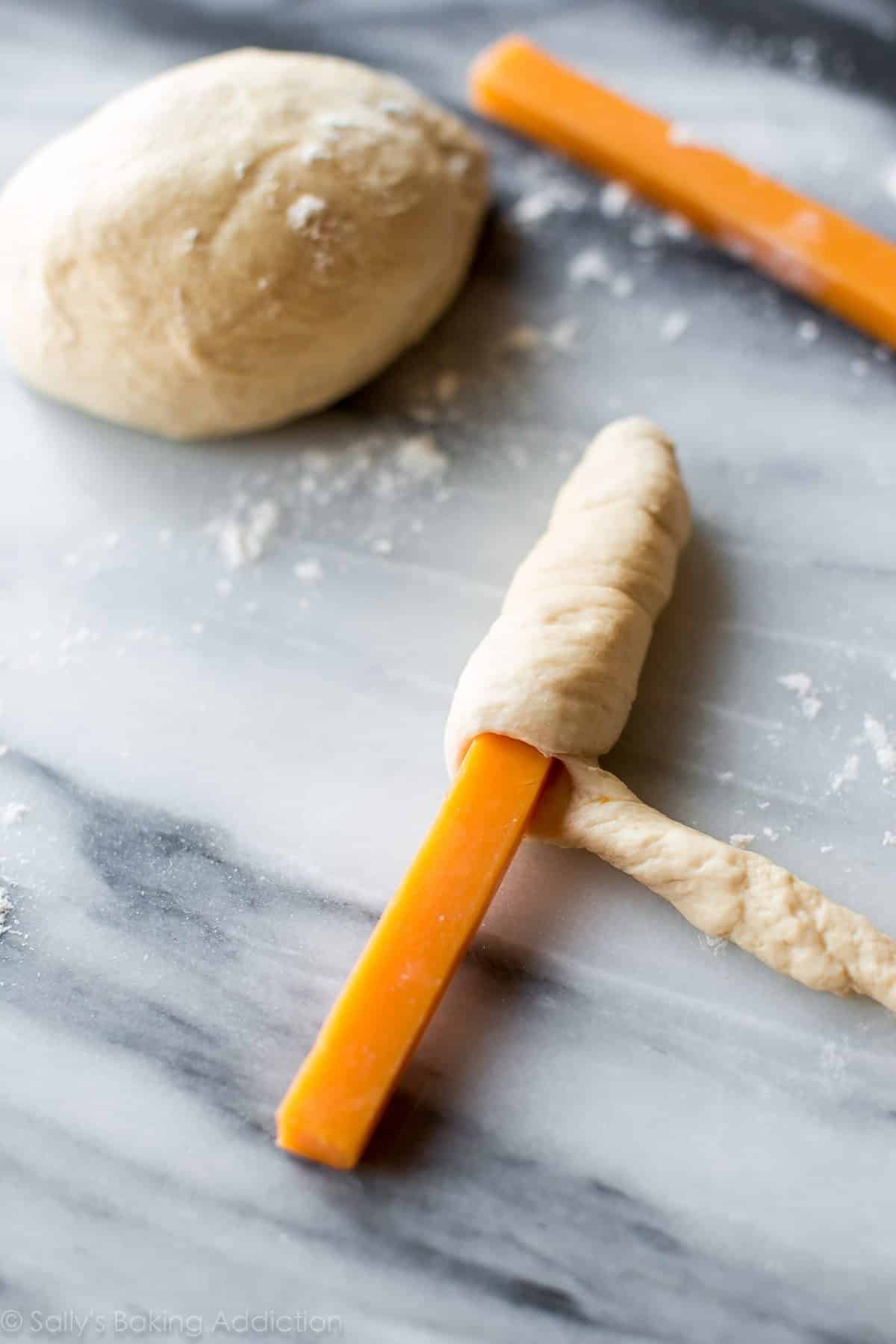 wrapping piece of cheddar string cheese with pretzel dough