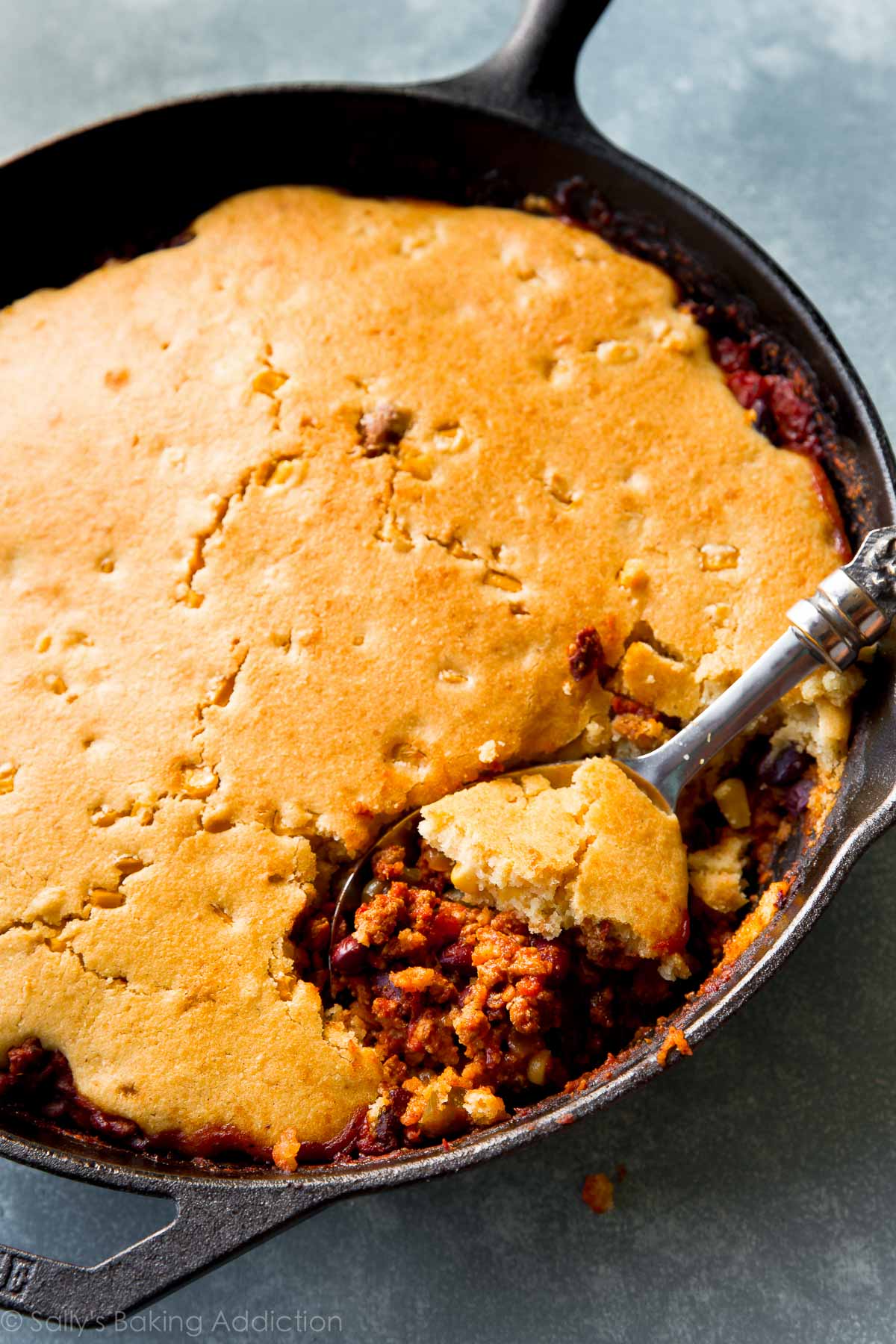 chili in a skillet topped with cornbread with a serving spoon