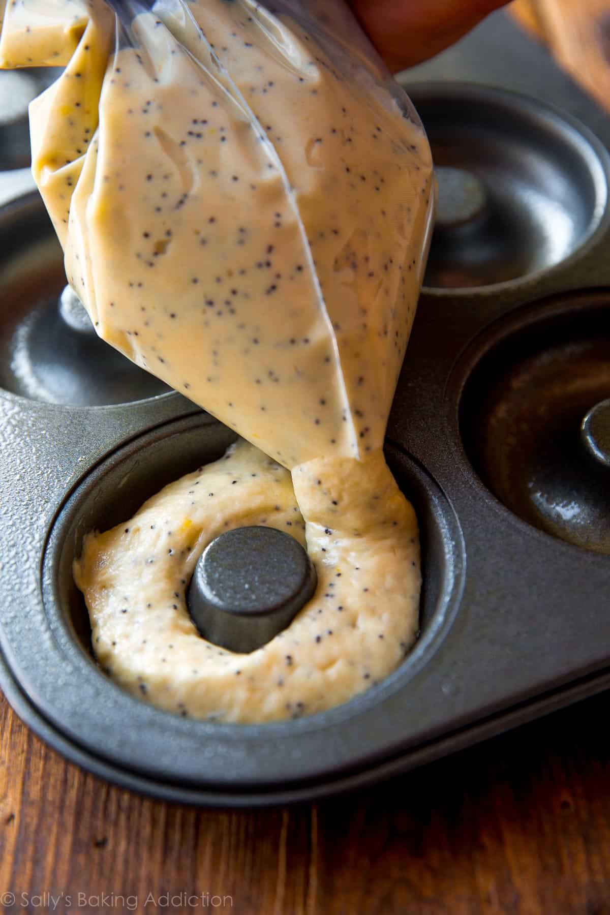 piping lemon poppy seed donut batter into a donut pan