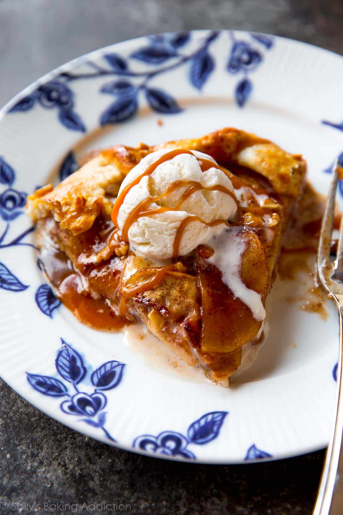 slice of salted caramel apple galette with a scoop of vanilla ice cream on a blue and white plate with a fork