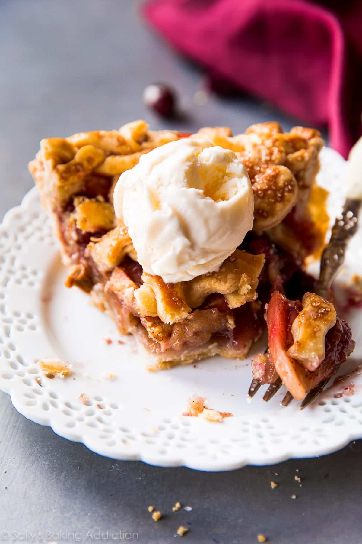 slice of apple cranberry pie with a scoop of ice cream on a white plate with a fork