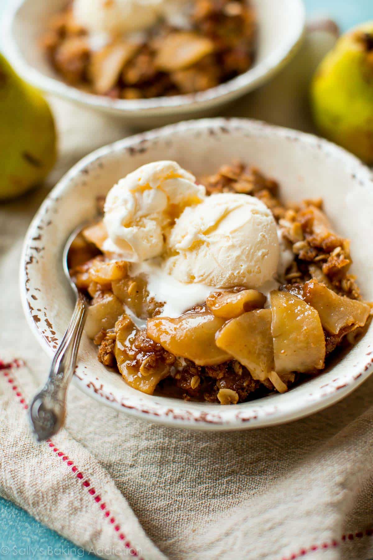 serving of apple pear crisp in a white bowl with a scoop of vanilla ice cream on top and a spoon