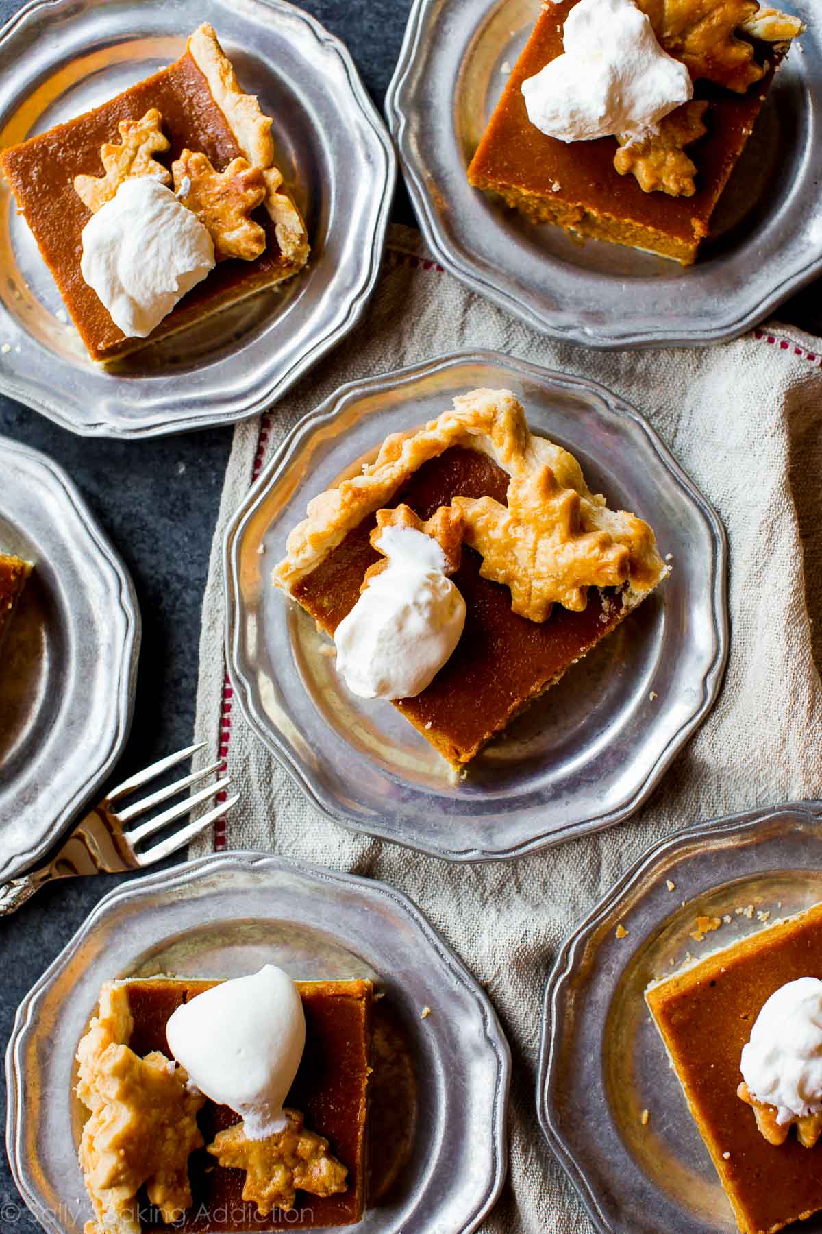 overhead image of slices of pumpkin slab pie with whipped cream on silver plates with a fork