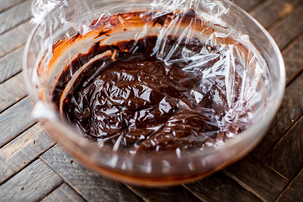 chocolate hazelnut truffle filling in a glass bowl with a piece of plastic wrap pressed on top of the filling to cover it completely