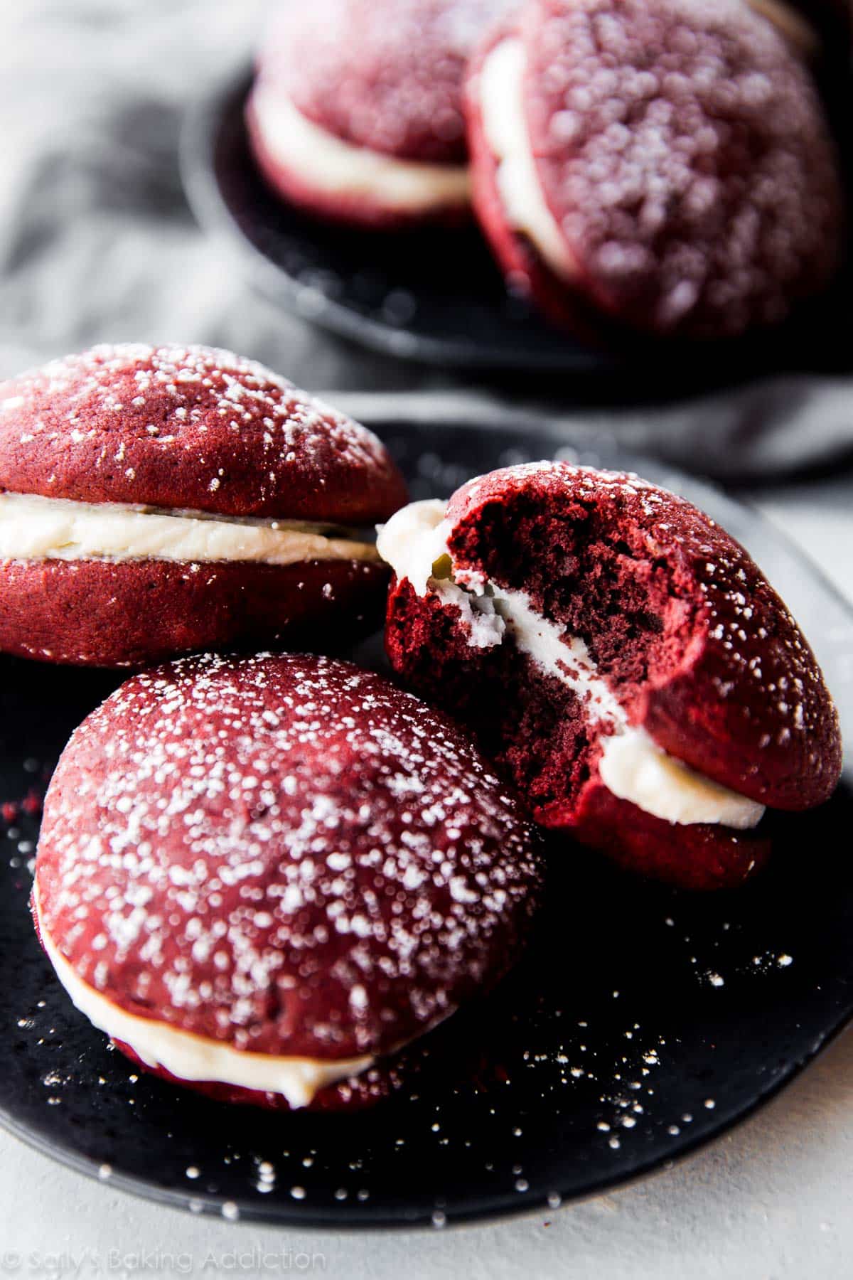 red velvet whoopie pies on a black plate with a bite taken from one whoopie pie
