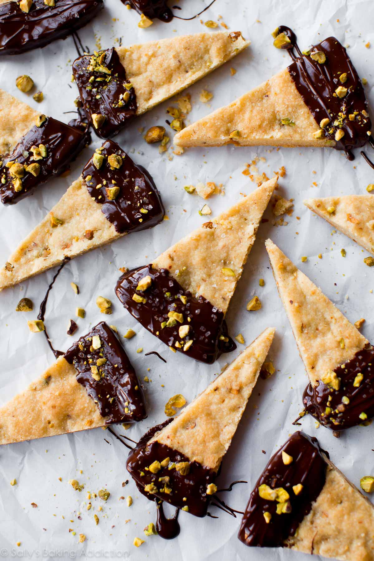 overhead image of pistachio shortbread triangles with the ends dunked into dark chocolate and sprinkled with sea salt and crushed pistachios
