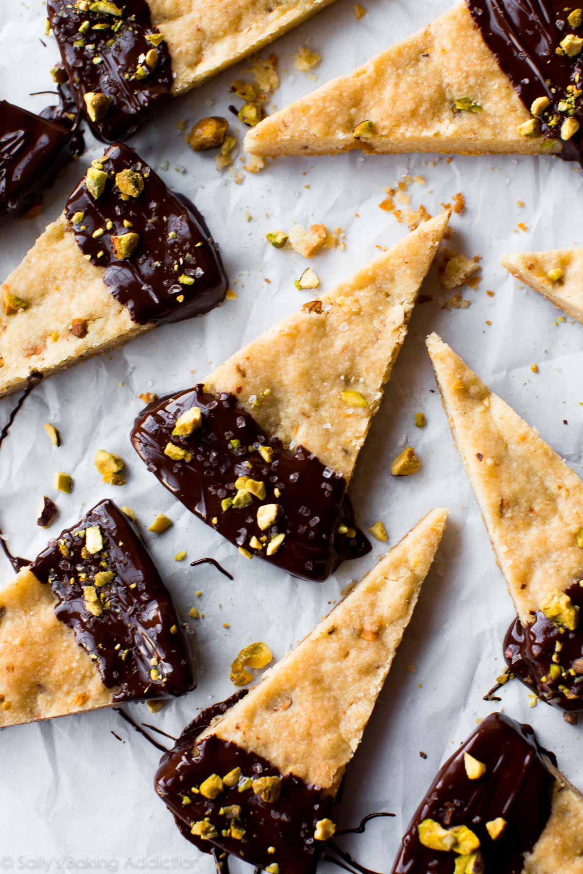 overhead image of pistachio shortbread triangles with the ends dunked into dark chocolate and sprinkled with sea salt and crushed pistachios