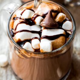 glass mug of hot chocolate topped with marshmallows, chocolate sauce, and a Hershey's kiss