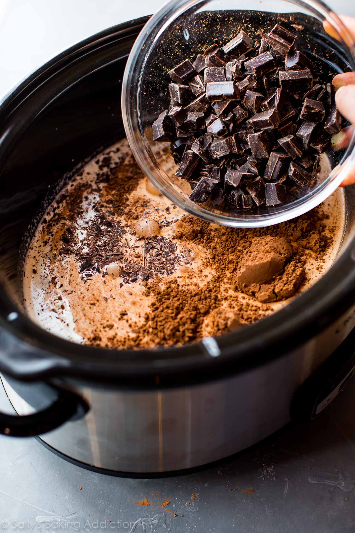 pouring chocolate chunks into slow cooker with other hot chocolate ingredients