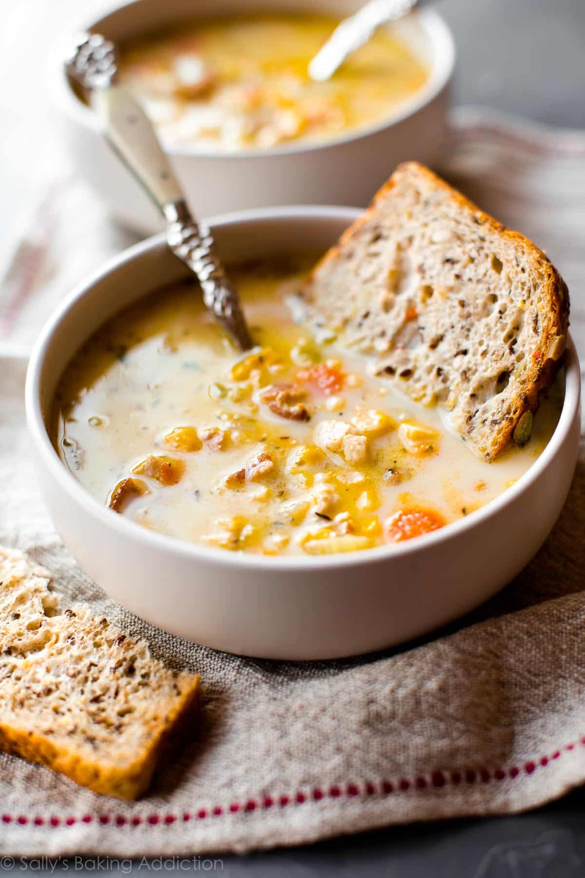 chicken chowder in a white bowl with a slice of bread and a spoon