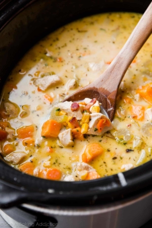 chicken corn chowder in a slow cooker with a wood spoon
