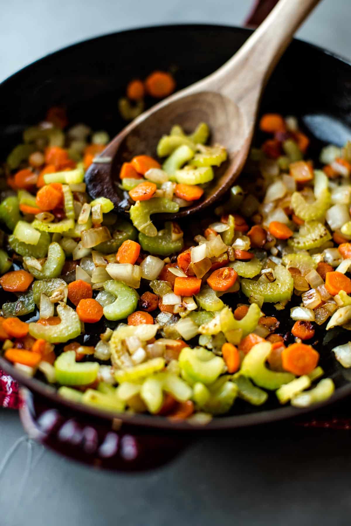 onion, celery, and carrots sautéed in a skillet with a wood spoon