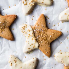 star shaped maple sugar cookies with half of each cookie dipped into white chocolate and topped with sprinkles on parchment paper