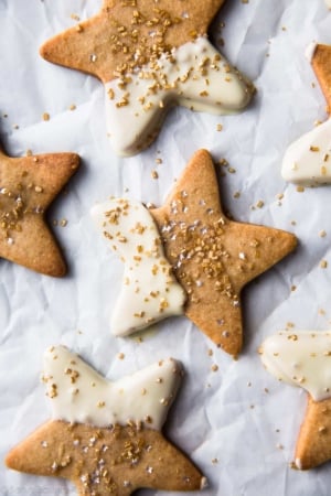 star shaped maple sugar cookies with half of each cookie dipped into white chocolate and topped with sprinkles on parchment paper