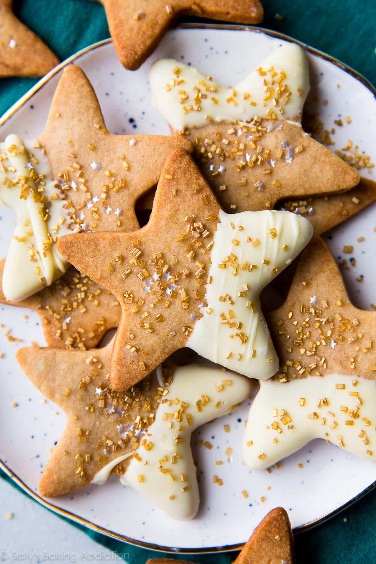 star sugar cookies with half of each cookie dipped in white chocolate and topped with gold sprinkles on a white plate
