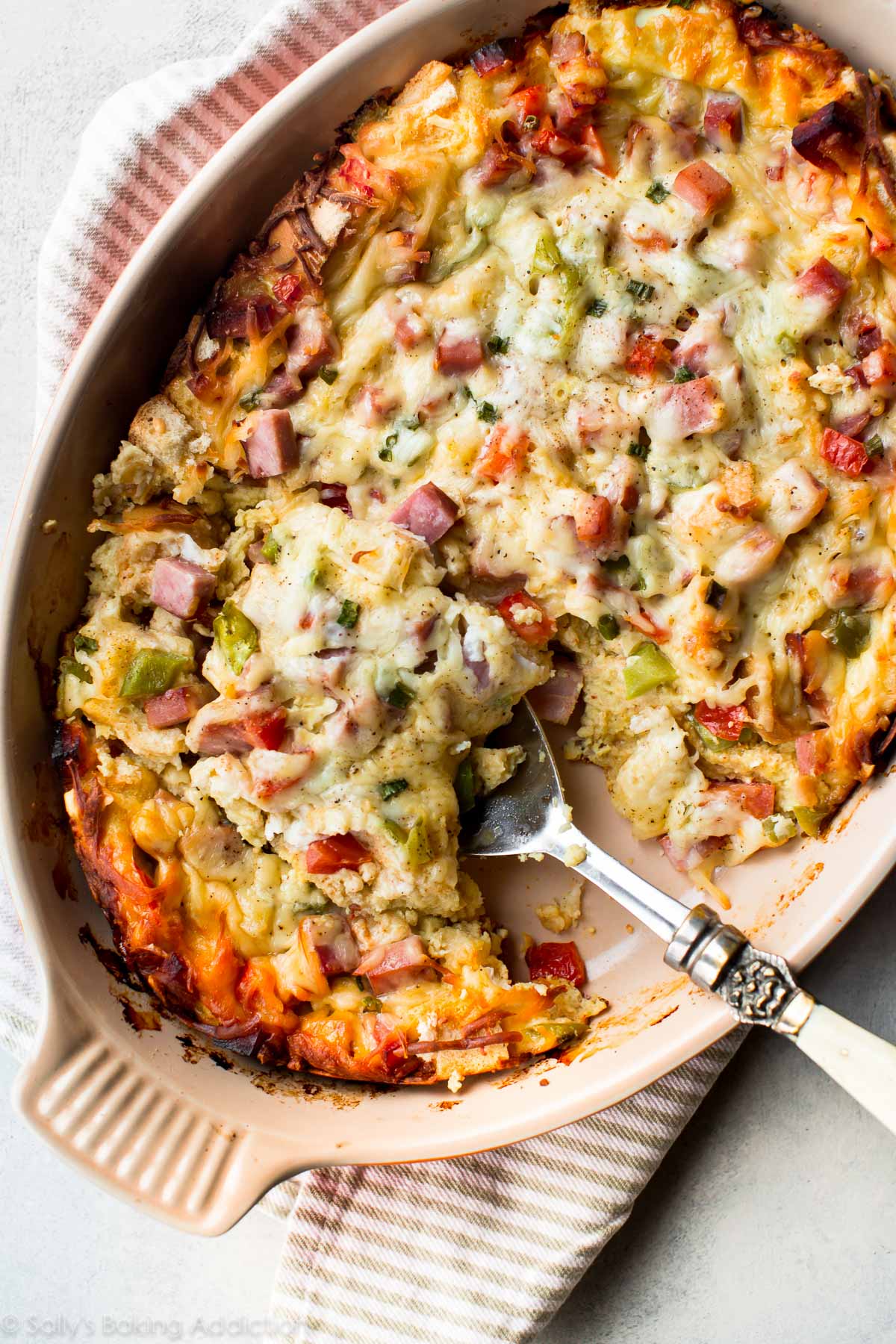 overhead image of ham and cheese strata in a casserole dish with a serving spoon